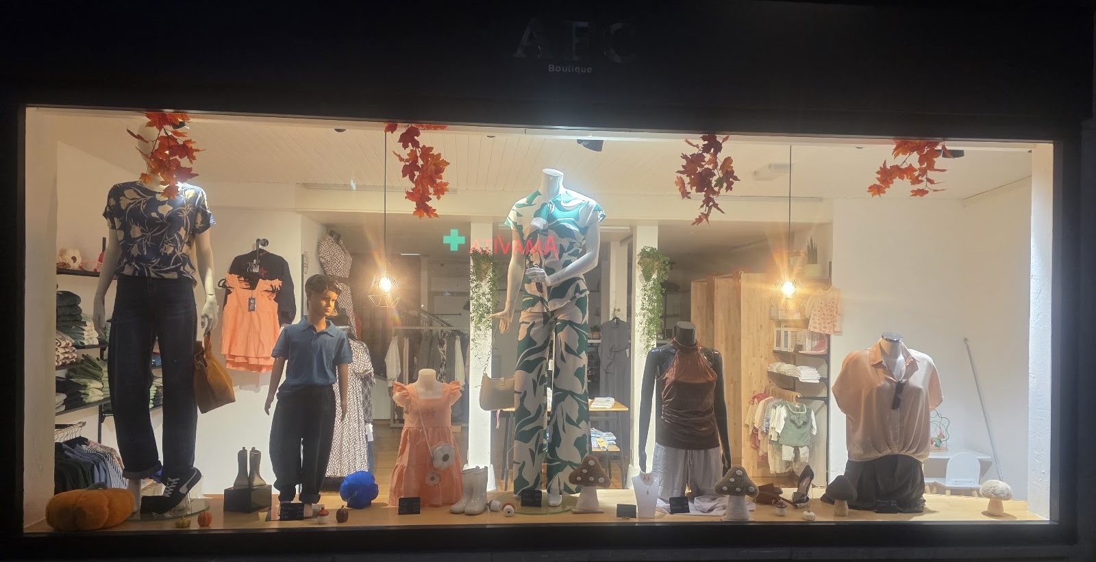 La vitrine d'AFC Boutique le soir : mannequins femme et enfant, chaussures, sacs et décoration d'automne.
